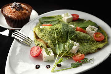 Breakfast. Omelet with spinach and cheese on a white plate, on a black background