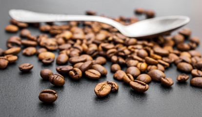 Heap of coffee beans with teaspoon on black.