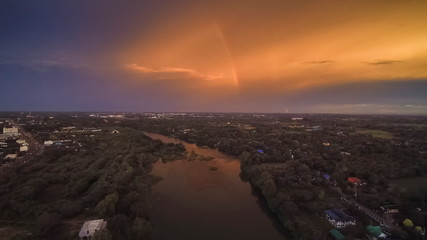Aerial view sunset above Mae Klong River around with green forest on both bank with yellow sun light and rainbow in cloudy sky background, Ban Pong, Ratchaburi, Thailand.