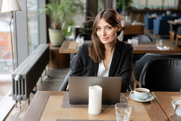 Lovely young woman Sitting in coffee shop. On table is gray aluminum laptop. Girl blogging, browsing internet, chatting in social networks. Uses a wireless Internet connection