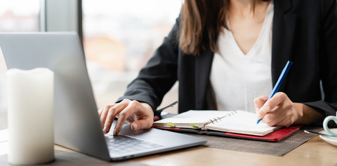 Southpaw write in a notebook. Close-up hand of a woman making notes in a notebook. Young businesswoman Sitting in coffee shop at wooden table. Schedules and makes important notes