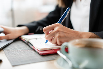Southpaw write in a notebook. Close-up hand of a woman making notes in a notebook. Young businesswoman Sitting in coffee shop at wooden table. Schedules and makes important notes