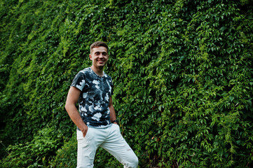 Lifestyle portrait of handsome man posing against greenery wall.