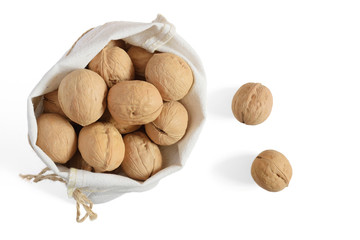 Walnuts in reusable natural cotton bag and two scattered walnuts, isolated on white background. Full bag of nuts. Top view. All objects are in focus