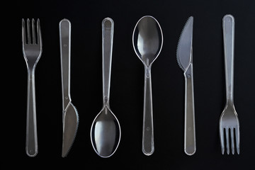 Transparent plastic spoons, knives and forks on black background. Clear disposable cutlery set. Top view