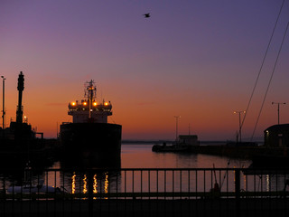 Silhouette of a cargo ship at port at sunset of sunrise. Orange purple tones. Vessel lights...
