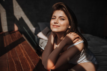 Portrait of a cute girl in the morning by the window on the bed in the sunlight