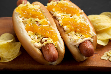 Homemade colombian hot dogs with pineapple sauce, chips and mayo ketchup on a rustic wooden board on a black background, side view. Close-up.