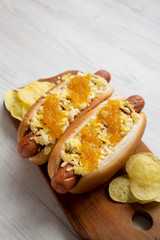 Homemade colombian hot dogs with pineapple sauce, chips and mayo ketchup on a rustic wooden board on a white wooden surface, side view. Space for text.