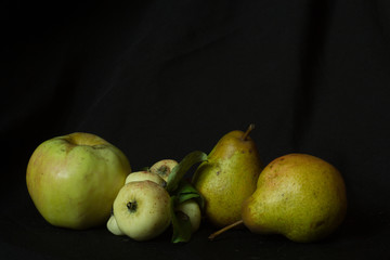 Fototapeta na wymiar An apple, two pears and small wild apples on a black background, autumn still life