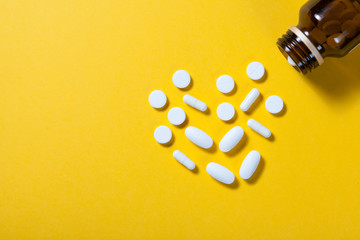 Pill bottle spilling pills on to surface on yellow background