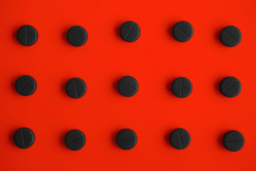 Black tablet pills on a red background. Top view. Flat lay