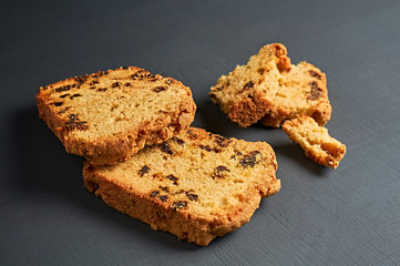 Scattered pieces of tasty sweet homemade bread with raisin lies on dark concrete table in kitchen. Close-up