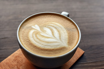 Close up of cup of coffee on wooden table with heart pattern on top. Selective focus.