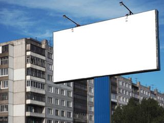 Empty weathered wooden billboard on a metal stand against slightly blurred old multistory apartment house and cloudy blue sky. Blank white advertising panel. Copy space