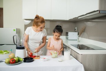 Obraz na płótnie Canvas Cute little girl and her mom in chef's hats are cutting vegetables cooking a salad and smiling