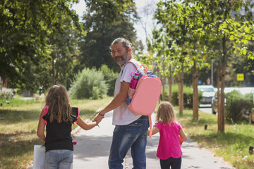 Fototapeta premium Father is taking his daughters to school, wearing kids schoolbag on his back