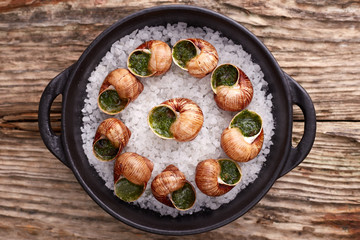 Escargots de Bourgogne - Snails with herbs butter on wooden background. Salad. Parsley.