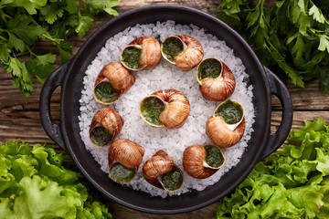 Escargots de Bourgogne - Snails with herbs butter on wooden background. Salad. Parsley.