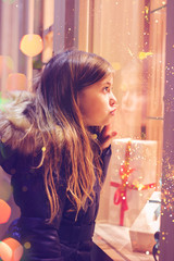 Beautiful little girl in front of confectionery shop, decorated with wrapped gift boxes and candies. Christmas concept, window shopping