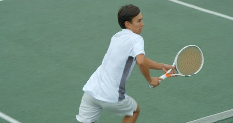 A tennis player runs across court close to the net, hits a backhand and smiles.