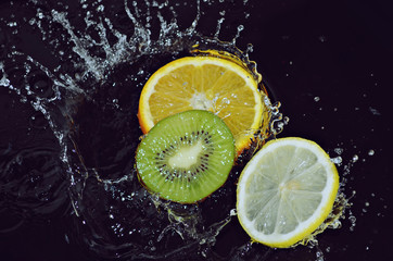 Slices of fruit in water with splashes on a black background