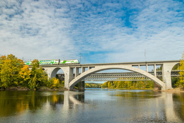 Fototapeta premium Kouvola, Finland - 25 September, 2019: Autumn landscape of bridge with moving passenger train and Kymijoki river waters in Finland, Kymenlaakso, Kouvola, Koria