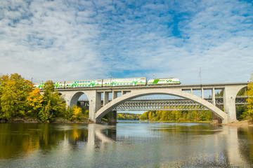 Naklejka premium Kouvola, Finland - 25 September, 2019: Autumn landscape of bridge with moving passenger train and Kymijoki river waters in Finland, Kymenlaakso, Kouvola, Koria
