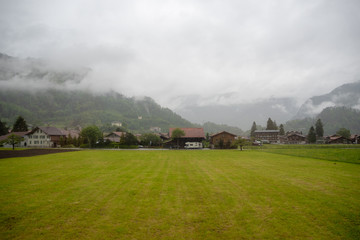 Fototapeta na wymiar Beautiful scene of houses and field in rural area of switzerland on foggy mountain background and copy space