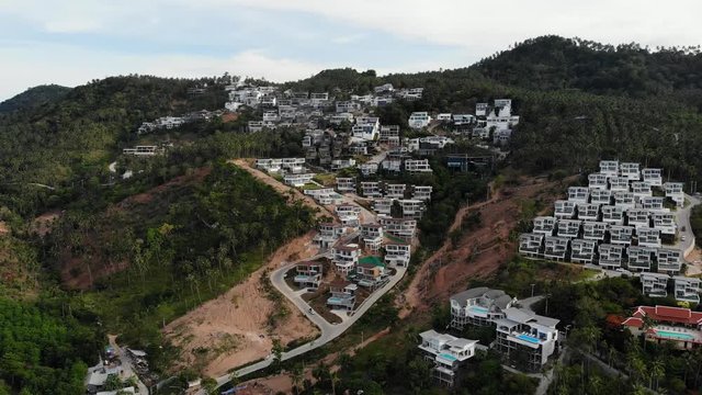 Tropical terrain covered with endangered forests and luxury villas. Drone view of large tropics with ecosystem disturbance due to buildings and deforestation. Koh Samui. Coconut palm plantations