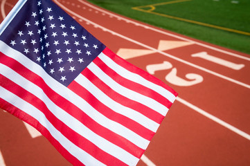 Fototapeta na wymiar American flag flying over the numbered lanes of an athletic running track
