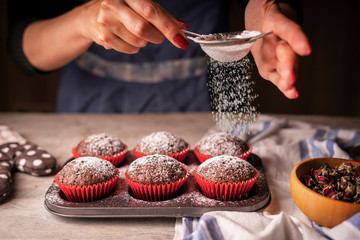 Female hands sprinkle icing sugar with chocolate muffins.