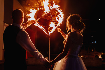 Fire show at the wedding. The bride and groom on the background of a fiery heart and fireworks and fireworks