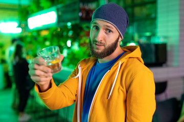 Man with a glass of whiskey alcoholic drink offers to drink more while standing at the bar.