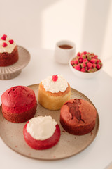 Various muffins on white plate with a bowl of raspberry and cup of coffee