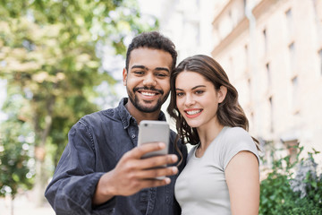 Beautiful happy couple using smartphone. Young joyful smiling woman and man looking at mobile phone in a city. Technology, travel, students concept