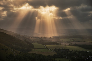 Stunning Summer landscape image of escarpment with dramatic storm clouds and sun beams streaming...
