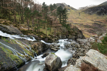 Stunning landscape image of Ogwen Valley river and waterfalls during Winter with snowcapped mountains in background