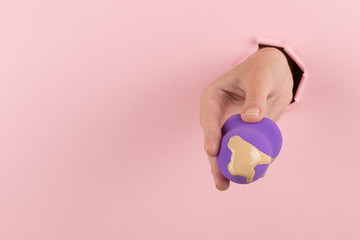 Girl hand holds a beauty blender in foundation, concealer from a hole in a pink background. Makeup artist concept, copy space.