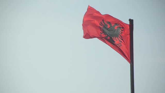Albanian national flag flying on a flagpole against blue sky. State and national symbol. Albanian flag waving in the wind. Republic. Shqipëri. Red flag with black double-headed eagle. Flamuri Kombëtar