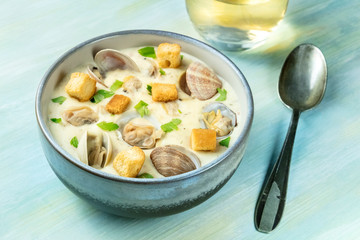 Clam chowder with fresh parsley and croutons, with a glass of wine, on a blue background