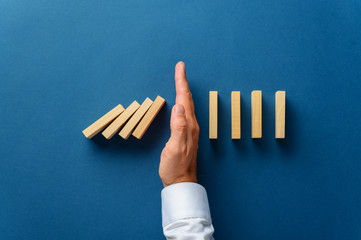 View from above of male hand interfering collapsing dominos - obrazy, fototapety, plakaty