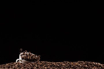 A cup with coffee beans in the air flying in flight like a spray. On a black background, coffee shop advertising concept, copy space.