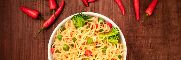 A panorama of soba noodles with green vegetables, shot from the top on a dark rustic wooden background with red peppers and a place for text