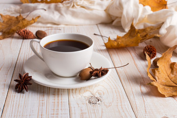 Fototapeta na wymiar White scarf, cup of coffee and dry yellow leaves on a wooden table. Autumn mood, copy space.