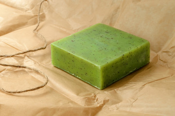 Green handmade herbal soap bar on a brown wrapping paper. Natural toiletries and hygiene products with herbs and essential oils.