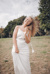 Fototapeta na wymiar Blonde happy girl laughs and runs on the grass. The girl in a white sundress laughs and enjoys life. Lifestyle in nature.