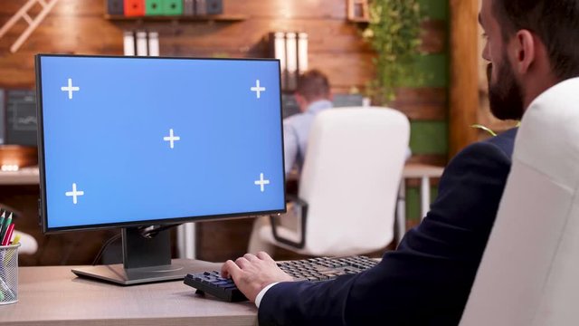 Back view of businessman in his office typing on computer with green screen.