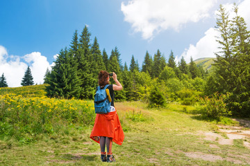 Fototapeta premium Woman wanderlust photographing scenery nature landscape on smartphone in the forest. Young female taking photo on cellular. Nature photographer tourist shoots while standing on top of the mountain.