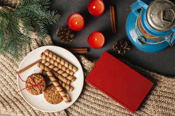  Red book, cookies on a plate and candles on a knitted blanket. winter cozy. Christmas background